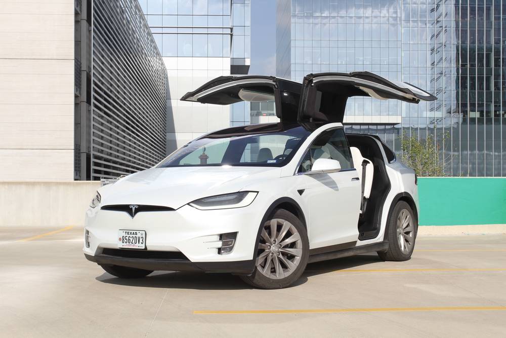 White Tesla Model X with its falcon doors raised on a rooftop deck